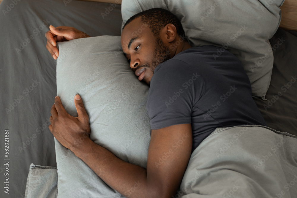 Fototapeta premium Tired African Male Lying Having Sleeplessness In Bedroom, High Angle