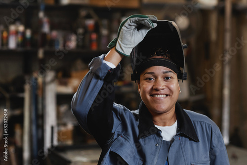 Closeup portrait of smiling female welder looking at camera in industrial factory, copy space