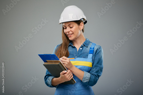 Woman engineer student in white helmet and overall writes on clipboard. Isolated female builder portrait.