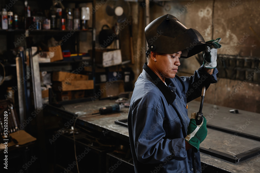 Side view portrait of woman welder inspecting tools in industrial workshop, copy space Side view portrait of woman welder inspecting tools in industrial workshop, copy space