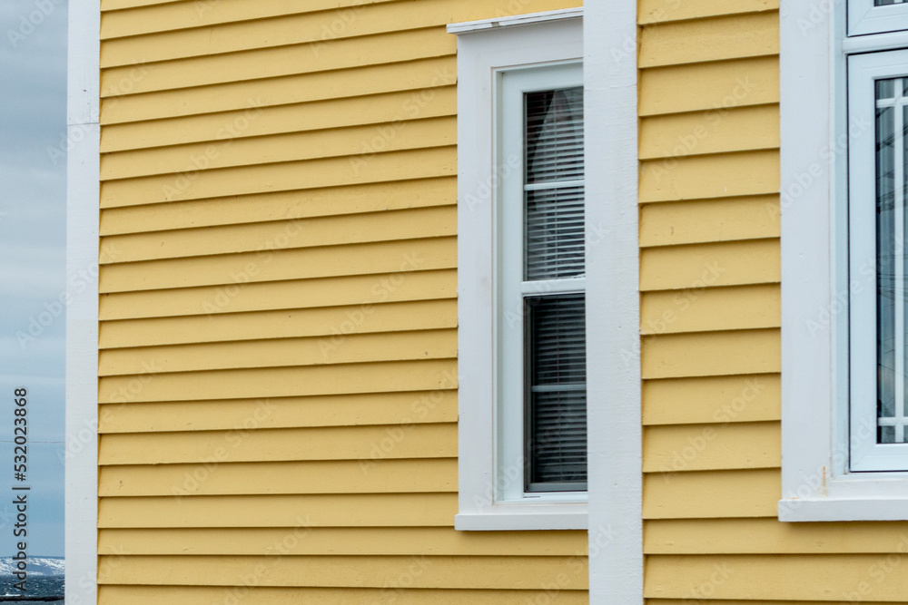 Fototapeta premium The exterior of a bright yellow narrow wooden horizontal clapboard wall of an old house with vinyl windows. The trim on the glass panes is white in color. The outside boards are textured pine wood. 