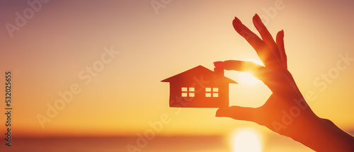 Tableau sur toile Woman's hand holding a model of a house on sunset evening