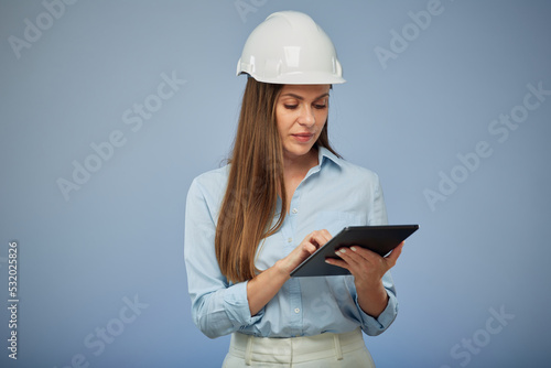 Smiling woman engineer in safety white helmet using digital tablet. Isolated female portrait on blue background.