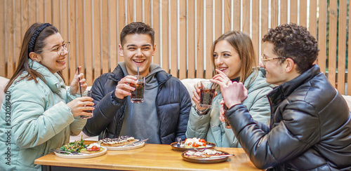 Group of teenagers having fun drinking and having brunch outdoors - Young people talking and laughing enjoing food drinks at a bar