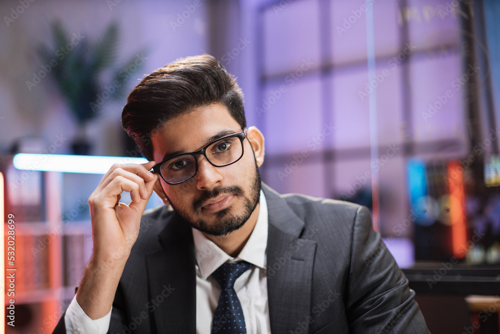 Close up portrait of confident indian businessman trader or economist in formal wear and glasses, posing on camera on night office. Close up portrait of confident indian businessman trader or economist in formal wear and glasses, posing on camera on night office.