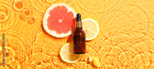 Fototapeta Naklejka Na Ścianę i Meble -  Bottle of citrus essential oil and fruits slices in water on orange background