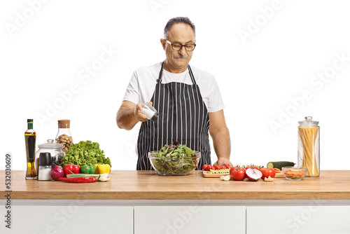 Mature man salting a salad on a kitchen counter
