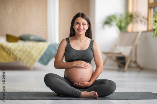 Beautiful Pregnant Woman In Activewear Sitting On Yoga Mat, Smiling At Camera