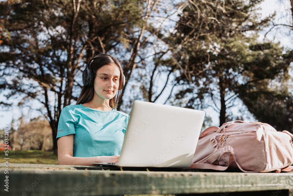 Smiling female university student using her laptop in campus natural park. E-learning concept. Smiling female university student using her laptop in campus natural park. E-learning concept.