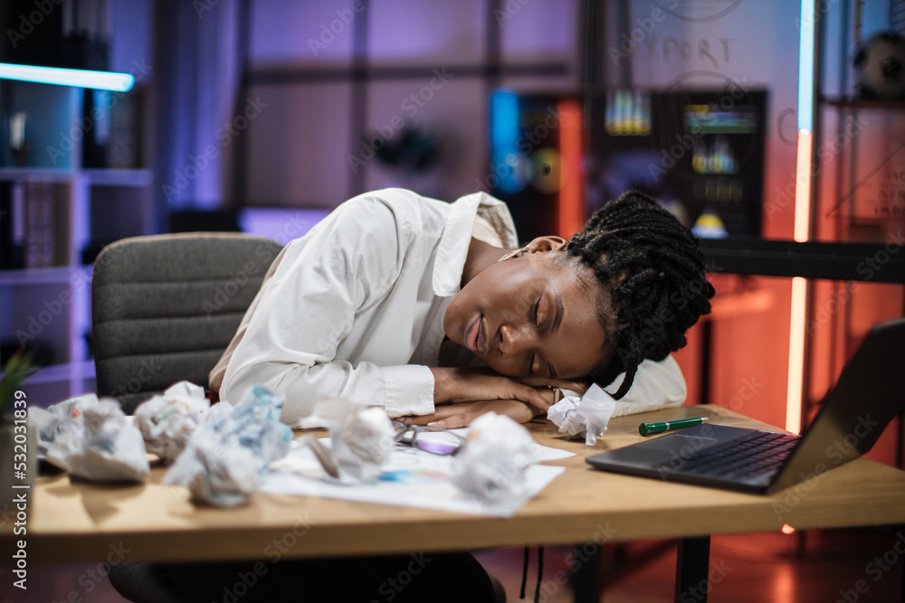 Portrait of tired overworked african american businesswoman in formal wear, sleeping on desk with sheets of crumpled papers in evening office. Portrait of tired overworked african american businesswoman in formal wear, sleeping on desk with sheets of crumpled papers in evening office.