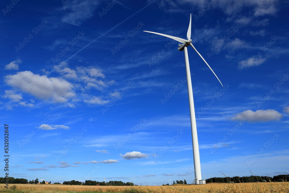 Fototapeta premium Wind power turbines at a meadow. Windy weather one summer day outside. Modern Swedish farm land. Near Skara, Sweden, Scandinavia, Europe. Year 2022.