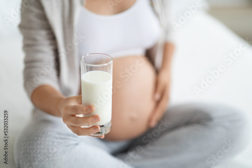 Unrecognizable pregnant woman holding glass of milk, cropped
