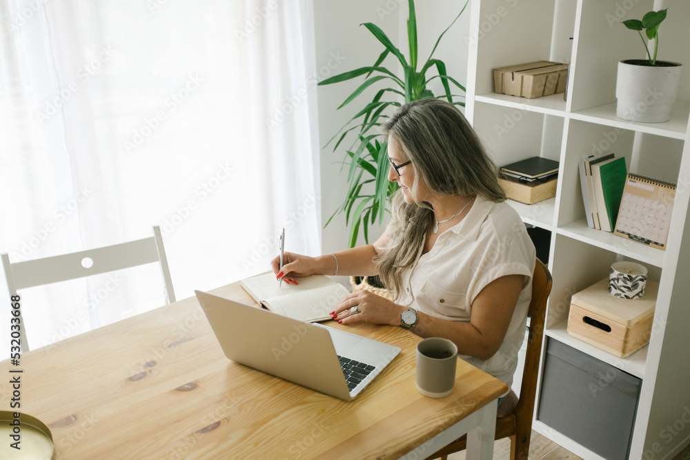 Caucasian woman sitting and writing in notebook at home Caucasian woman sitting and writing in notebook at home