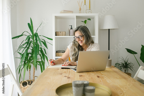 Smiling woman writing notes in notebook from browsing