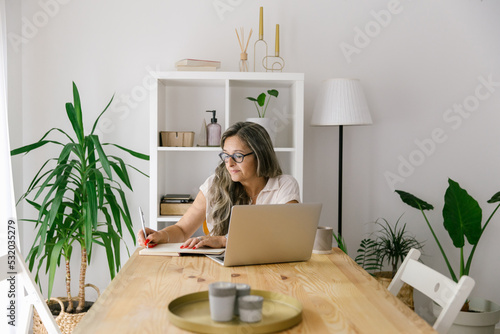 Mature woman taking notes from online webinar at home