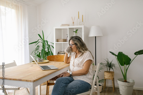 Mature woman in home office sipping coffee and browsing