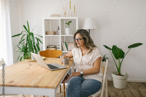 Woman sitting and reading from computer screen at home