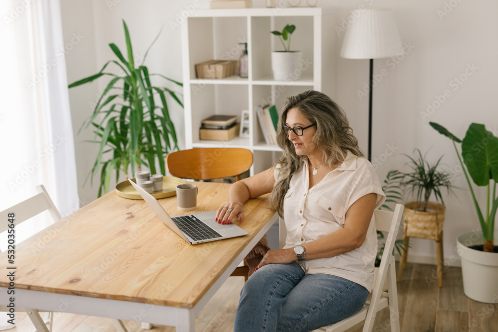 Mature woman sitting and working from home via laptop Mature woman sitting and working from home via laptop