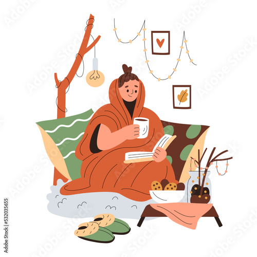 Smiling girl wrapped in a blanket sits in cushions and reads, holding a cup of warm drink