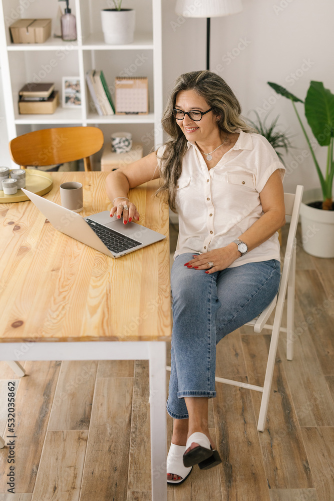 Smiling boomer woman browsing via laptop at home Smiling boomer woman browsing via laptop at home