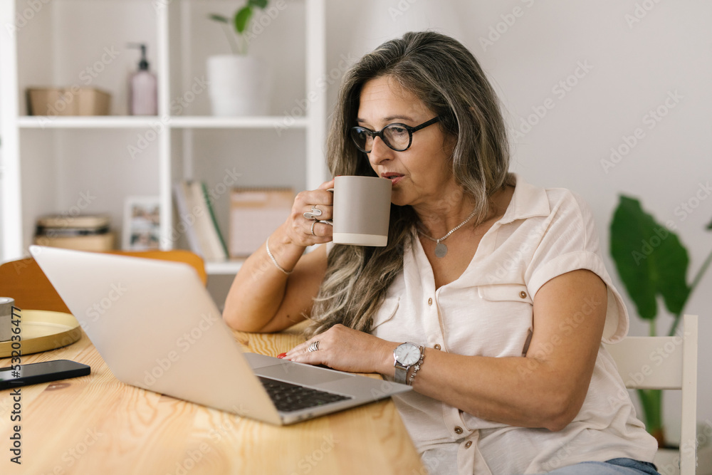 Woman sitting in front of laptop and sipping coffee Woman sitting in front of laptop and sipping coffee