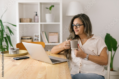 Woman holding cup of coffee and looking at the computer