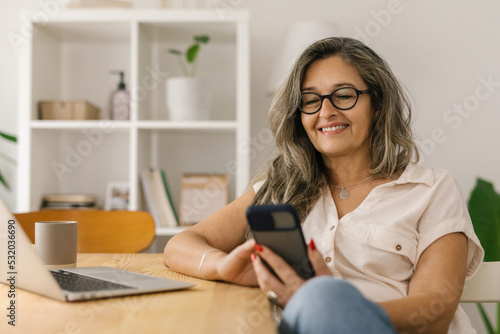 Happy woman sitting and using smart phone at home