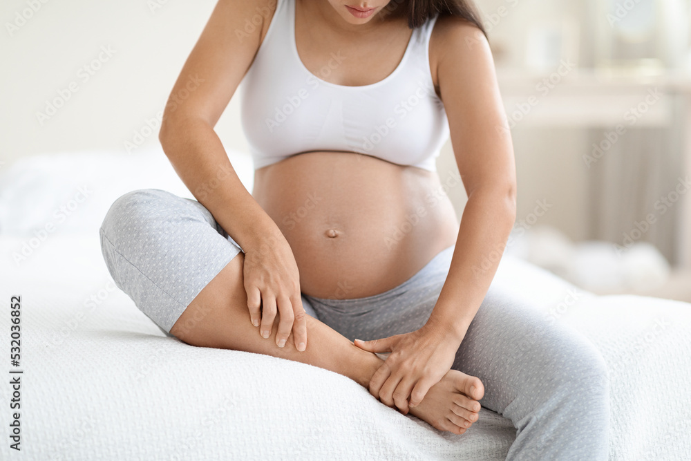 Pregnant woman massaging her swollen foot, sitting on bed Pregnant woman massaging her swollen foot, sitting on bed