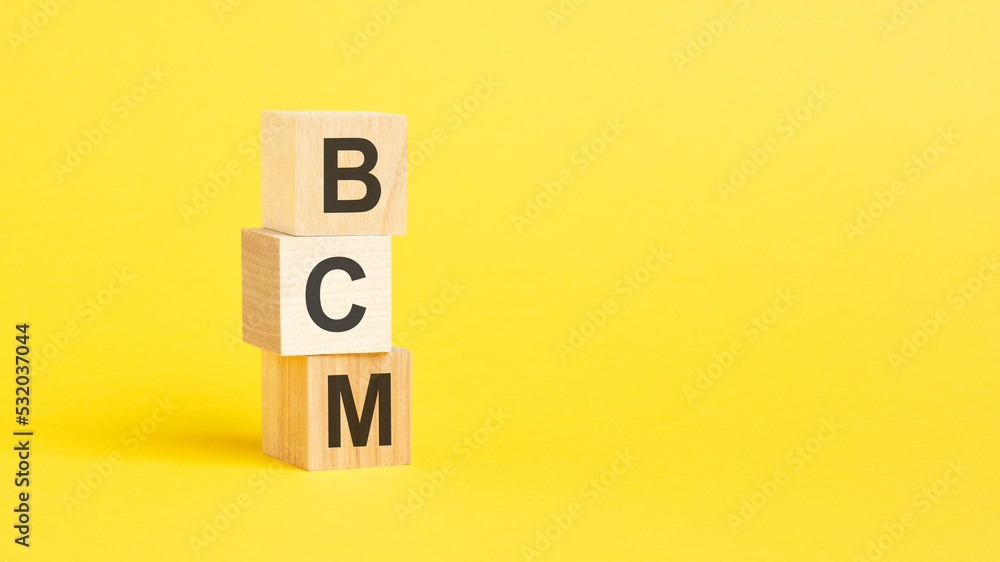 BCM - text on wooden cubes, on yellow background