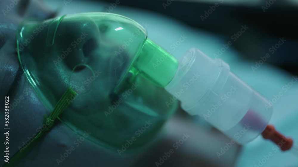 A female patient in medical mask is breathing oxygen support in a hospital with ecg heart rate machine. Unhealthy woman in coma. Getting mechanical ventilation. Concept of pandemic and therapy