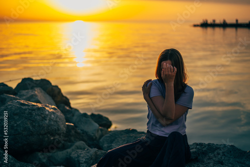 portrait of a woman hugging herself at sunset in the summer by the sea, covering her face with one hand