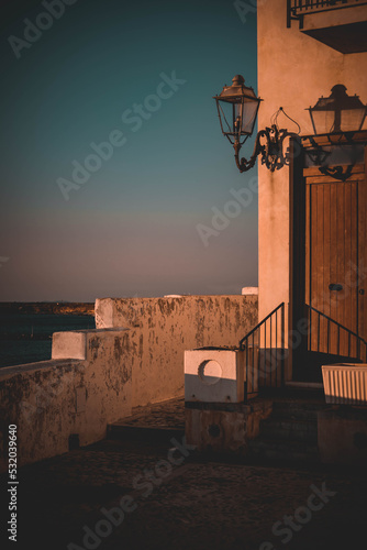 white italian house with wooden door and old street lamp on the coast during sunset