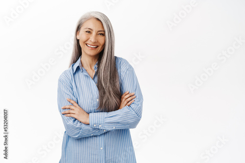 Smiling asian woman, senior lady looking with confidence, standing in power pose against white studio background