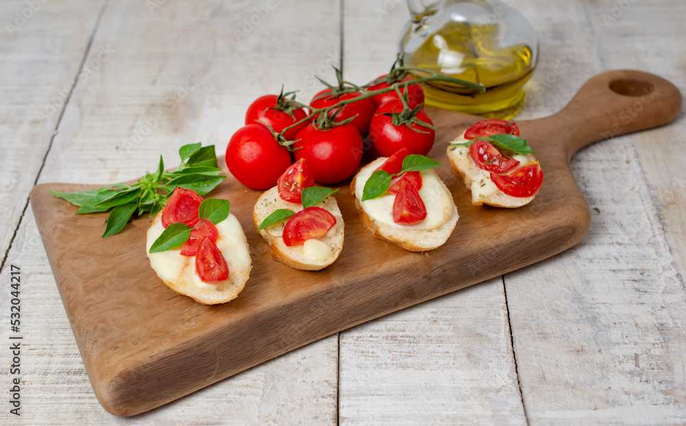 Homemade bruschetta with tomatoes, mozzarella cheese and basil on cutting board on a wooden background. Traditional italian appetizer or snack, antipasto. Top view, Homemade bruschetta with tomatoes, mozzarella cheese and basil on cutting board on a wooden background. Traditional italian appetizer or snack, antipasto. Top view,
