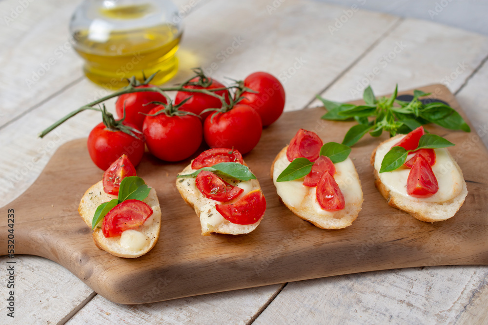 Italian homemade bruschetta with roasted cherry tomatoes, mozzarella cheese, basil and herbs on a cutting board Italian homemade bruschetta with roasted cherry tomatoes, mozzarella cheese, basil and herbs on a cutting board