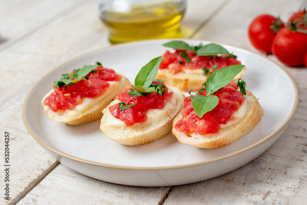 Traditional homemade roasted bruschetta with mozzarella, cherry tomatoes and basil in a white plate on a wooden background. Top view.