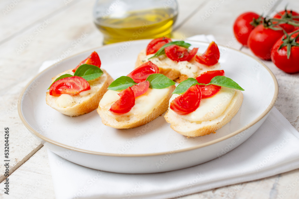 Traditional homemade roasted bruschetta with mozzarella, cherry tomatoes and basil in a white plate on a wooden background. Top view