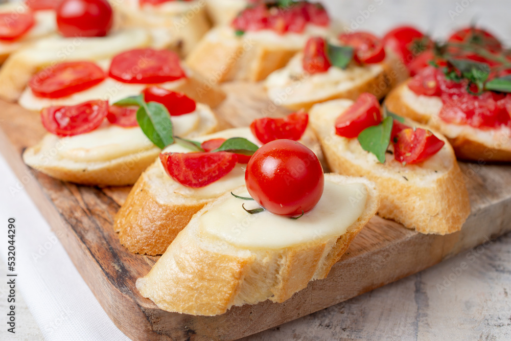 Italian homemade bruschetta with roasted cherry tomatoes, mozzarella cheese, basil and herbs on a cutting board