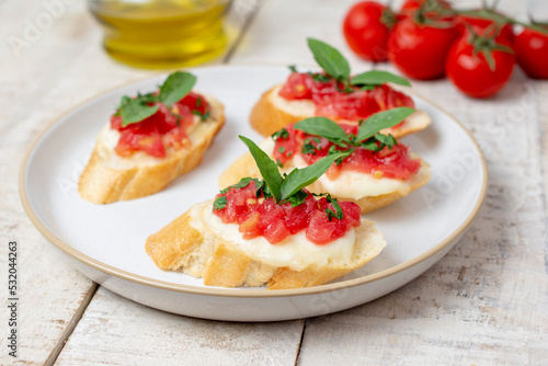 Traditional homemade roasted bruschetta with mozzarella, cherry tomatoes and basil in a white plate on a wooden background. Top view.
