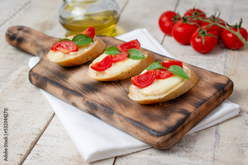 Italian bruschetta with roasted cherry tomatoes, mozzarella cheese and basil on a cutting board. top view