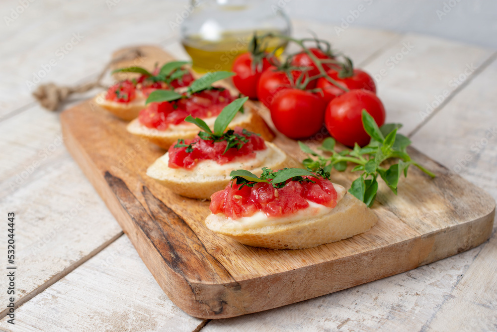 Homemade bruschetta with tomatoes, mozzarella cheese  and basil on cutting board on a wooden background. Traditional italian appetizer or snack, antipasto. Top view, flat lay.