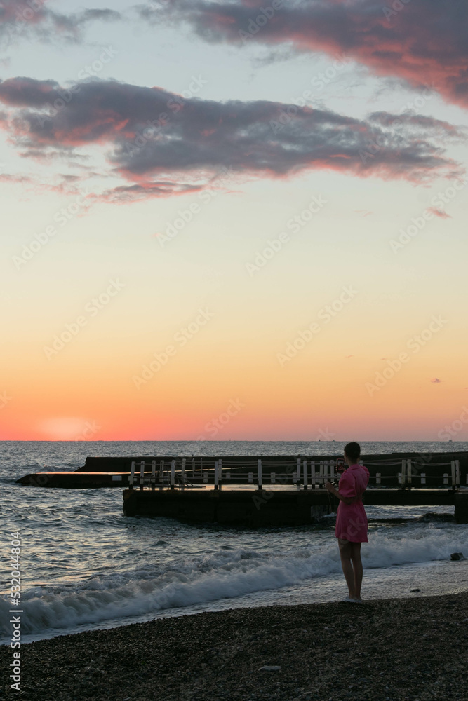 Fototapeta premium a girl takes a selfie on her phone on the seashore at sunset