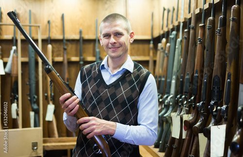 Portrait of confident smiling man standing in gun shop with hunting shotgun in his hands, happy with purchase
