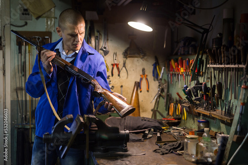 Gunsmith examines an automatic rifle before being repaired in a weapons workshop