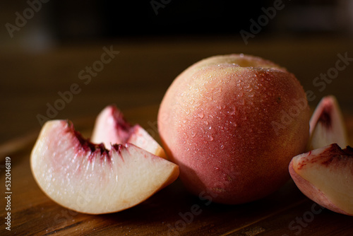 Organic White Peach with Peaches Sliced Next to it on Wooden Table and Dark Background. Fresh Fruit with Beads of Water. 