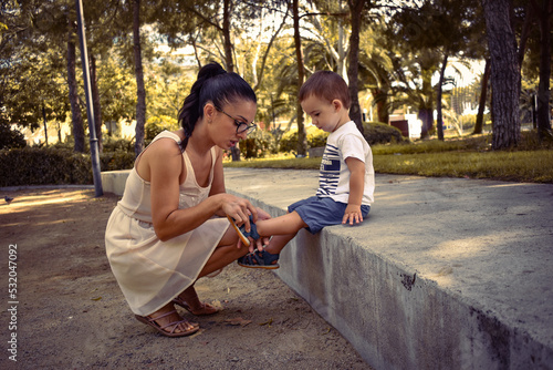 Mamá y bebé paseando por un jardín con palmeras y arboleda, hablando y mimándose