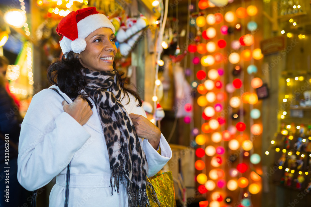 Hispanic woman standing at gift shop while visiting christmas fair and choosing christmas decorations.