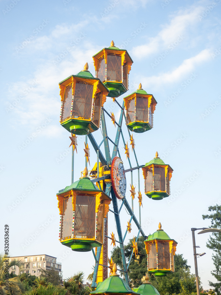 A small Ferris wheel in the park. A bright attraction for children. Entertainment in the park. Colorful booths. High above the ground. Children's fun. Entertainment industry concept.