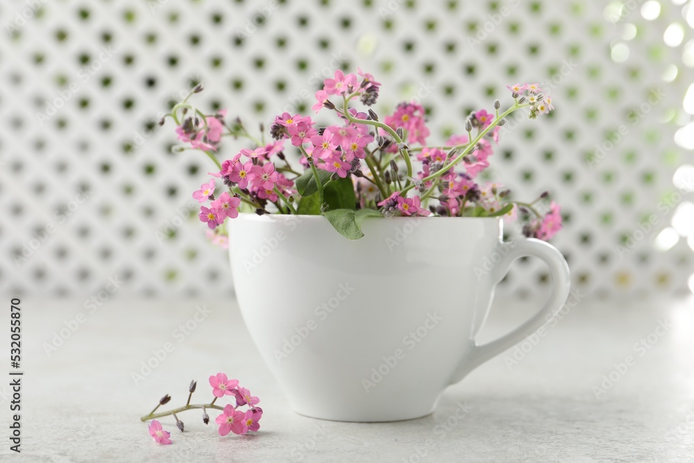 Beautiful pink forget-me-not flowers with cup on light stone table, closeup Beautiful pink forget-me-not flowers with cup on light stone table, closeup