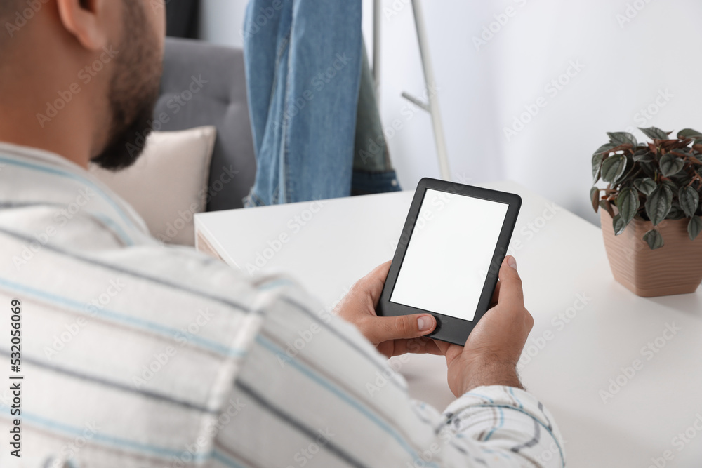 Man using e-book reader at white table indoors, closeup